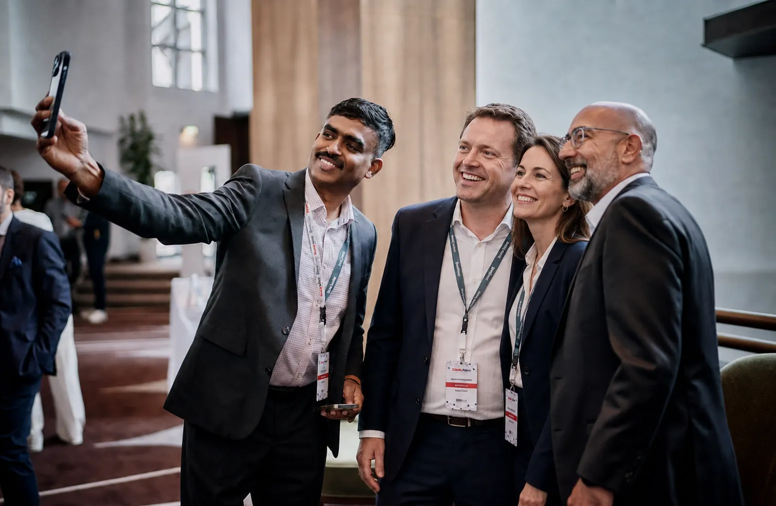 Four smiling professionals in business attire posing for a group selfie at a corporate event.